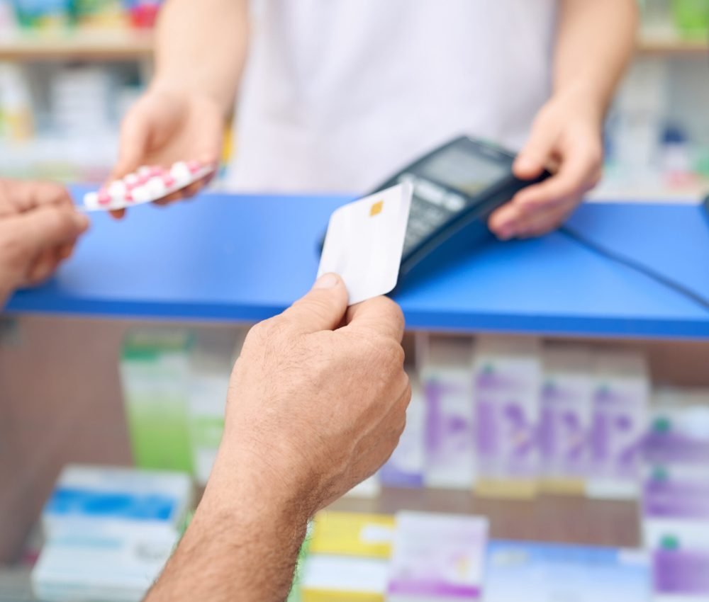 Crop of unrecognizable customer making payment in drugstore using credit card. Pharmacist holding terminal, man paying for medicaments. Moder payment machine, Blister pack of pills on counter.